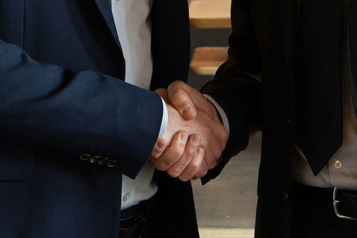 Two business professionals in suits shaking hands, symbolising negotiation, partnership, and trust in sports agency work.