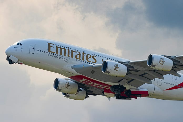 An Emirates Airbus A380 aircraft taking off, with its landing gear retracting and engines visible against a cloudy sky.