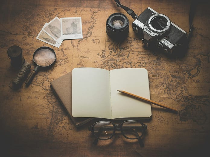 some tools like notebook, pen and camera are put over a map