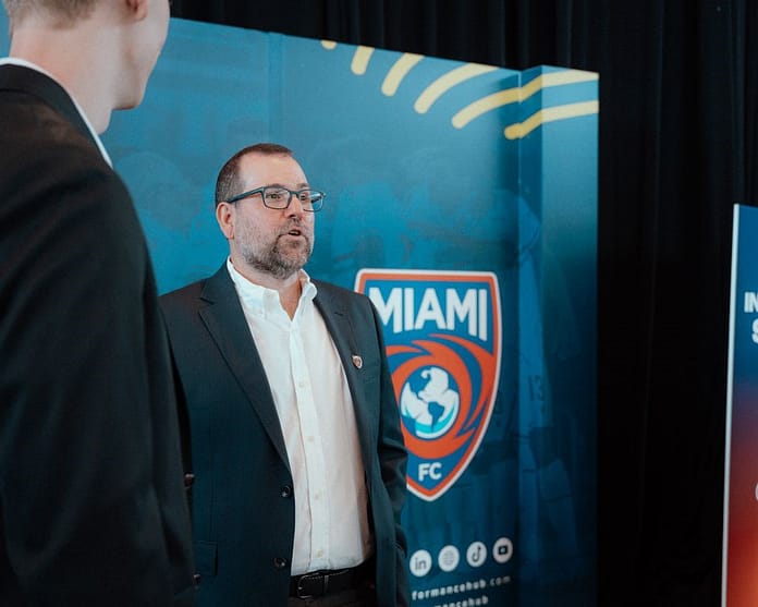Mario Roitman, President of Miami FC, speaks at a club event in front of the team’s logo backdrop.